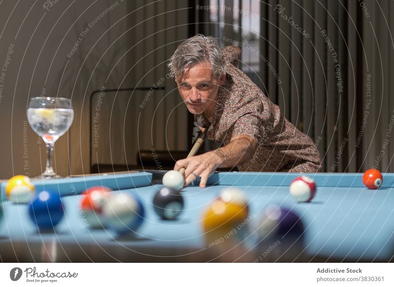 Concentrated player pushing ball with stick cue while playing pool man billiard leisure hobby game concentrate activity confident serious male gray hair pensive