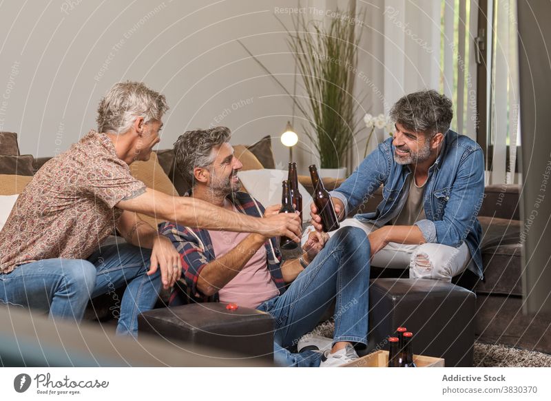 Happy mature friends cheering bottle while resting in room men cheers happy beer clink weekend friendship relax toast lounge living room fun together gather