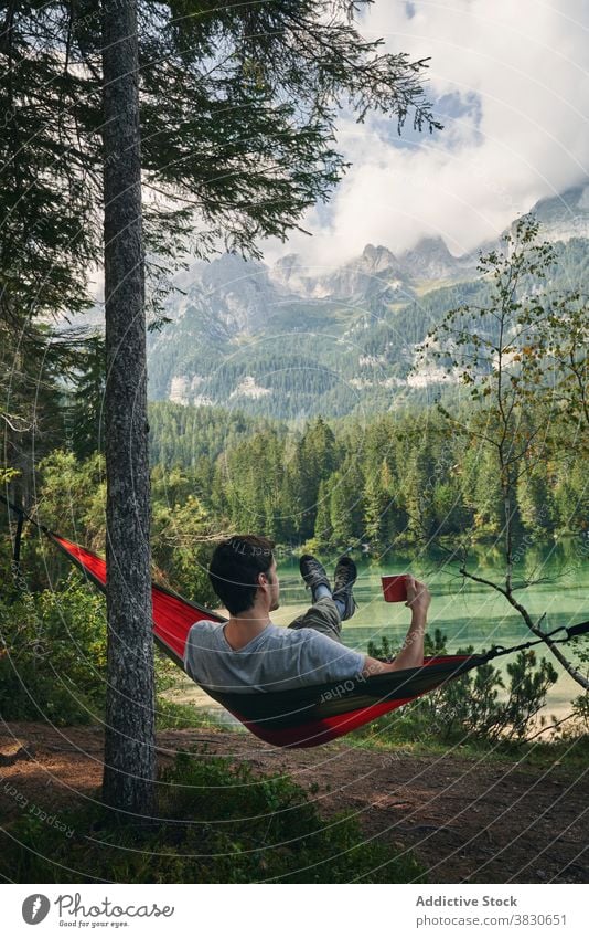 Man resting in hammock near lake surrounded by mountains man traveler relax journey nature vacation enjoy male tourism wanderlust tourist peaceful pond rock