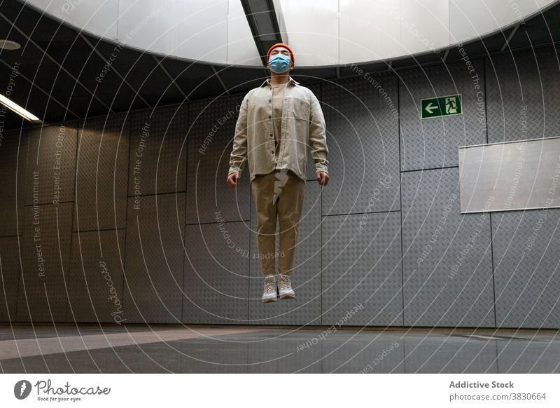 Calm Asian man levitating above floor in corridor jump above ground levitate calm hover serious mask hallway focus respirator concentrate thoughtful pensive