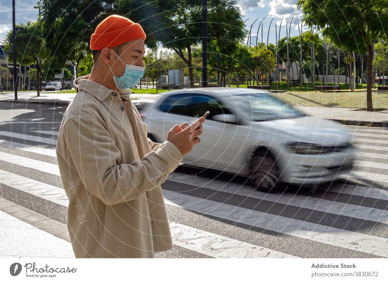 Calm Asian man browsing smartphone on street near moving car using crosswalk cellphone road sidewalk focus calm surfing gadget modern young casual mobile device