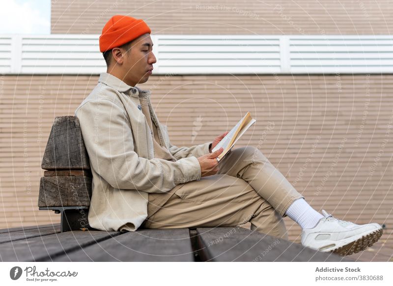 Concentrated Asian man reading book on street bench bookworm enjoy literature knowledge hobby concentrate serious education lifestyle focus study textbook