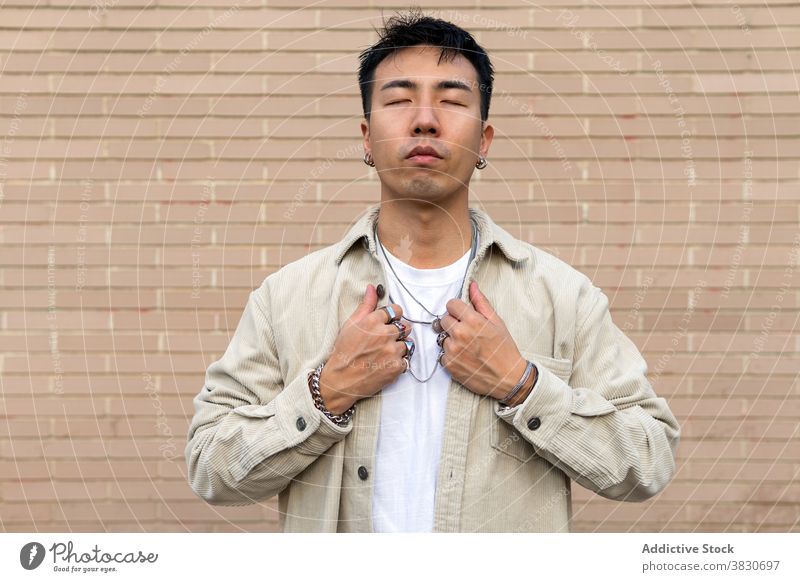 Pondering Asian man standing with eyes closed against brick wall ponder calm unemotional touch lapel thoughtful serious masonry pensive think casual contemplate