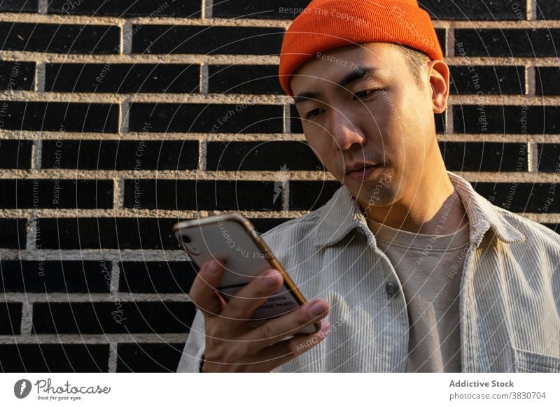 Dreamy Asian man taking on smartphone against brick wall content conversation phone call talk dreamy enjoy happy listen device gadget modern cheerful male