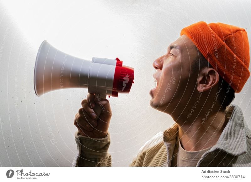 Expressive man shouting in megaphone against gray wall scream overwhelmed expressive loudspeaker darkness emotion exclaim voice yell call confident modern