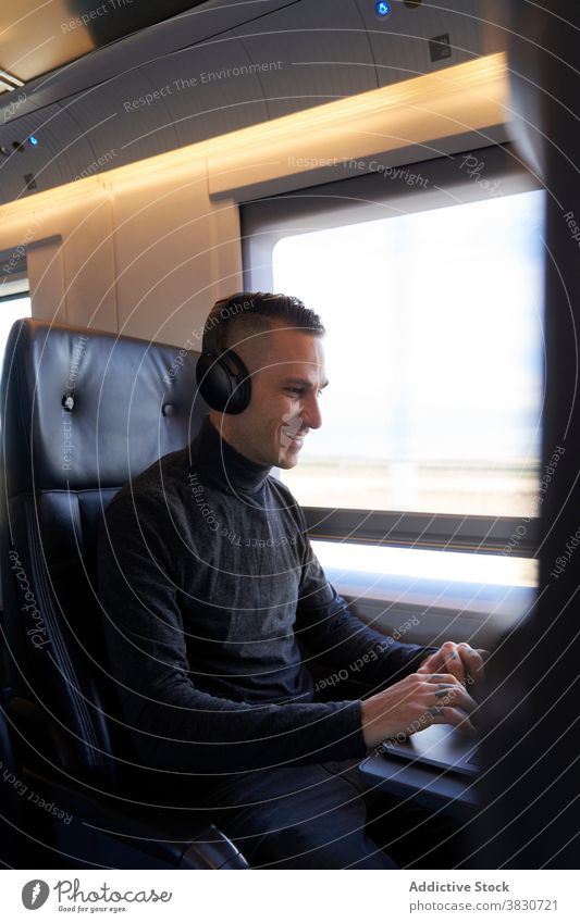 Man in headphones working on laptop in train business trip man freelance remote typing travel male seat modern passenger gadget device young netbook guy journey