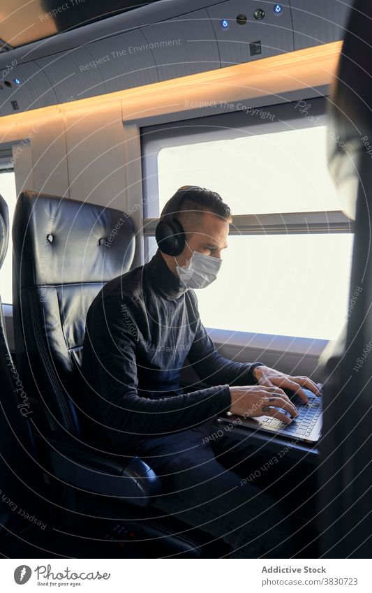 Man in mask using laptop in train man freelance project pandemic listen music male young headphones travel epidemic covid19 covid 19 coronavirus new normal