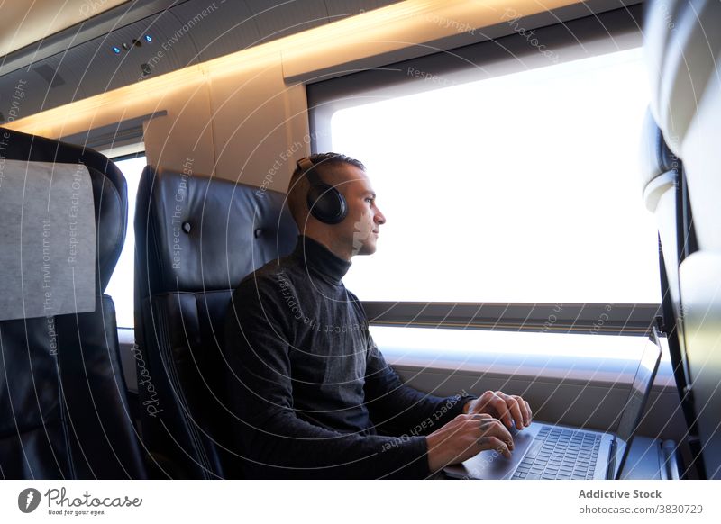 Man in headphones working on laptop in train business trip man freelance remote typing travel male seat modern passenger gadget device young netbook guy journey
