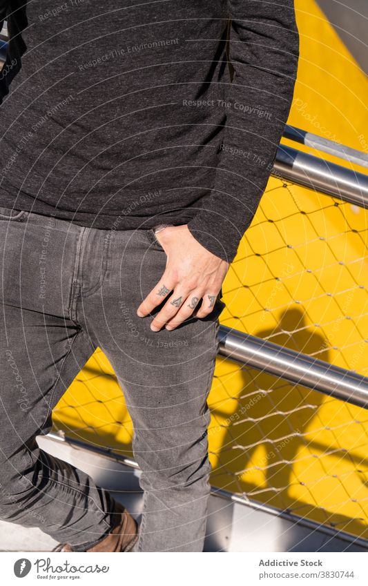 Young man with hand in pocket leaning on fence cool rest tattoo railing independent modern confident posture male young city guy metal lifestyle freedom jeans