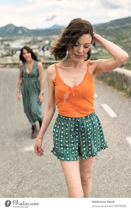 Skinny woman walking on road with friend stroll valley skinny slender touch hair style fashion mountain female shorts top sky hill slope dreamy smile summer