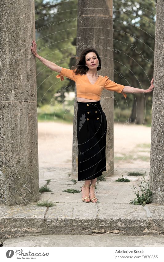 Gorgeous woman touching columns in park arms apart thoughtful slender outfit architecture exterior slim female beautiful crop top skirt apparel garment