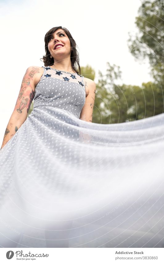 Cheerful woman in dress in park in daytime flying informal cheerful tattoo fashion gorgeous style slender female toothy smile content glad glamour apparel