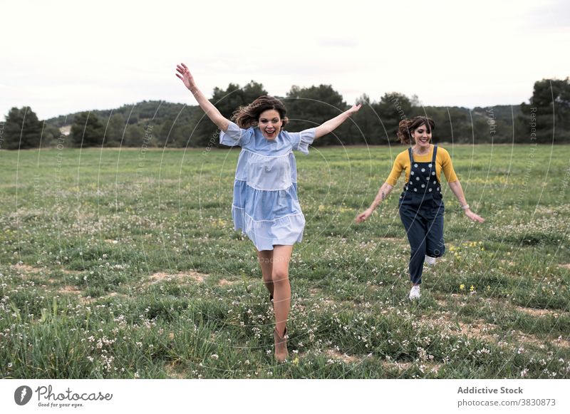 Positive women running through meadow happy excited carefree having fun summertime slender nature cheerful toothy smile harmony arms raised field friendship