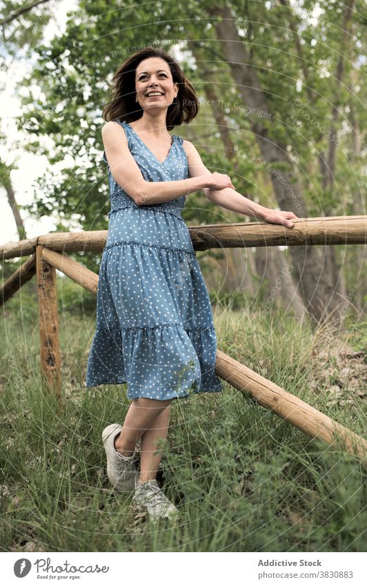 Dreamy woman standing near wooden fence on footpath forest park dreamy style fashion nature female dress dark hair appearance contemplate trendy daylight plant