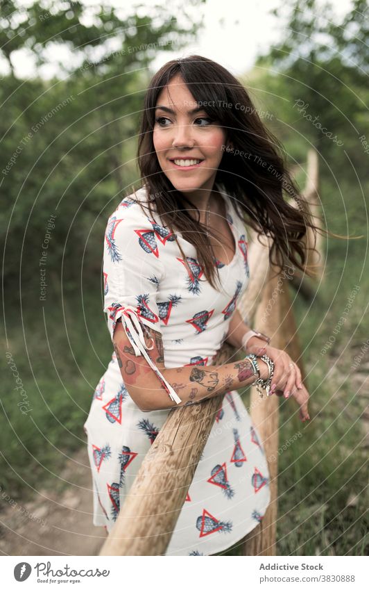 Dreamy woman leaning on wooden fence on footpath stand forest park dreamy style fashion nature female dress tattoo dark hair accessory appearance contemplate