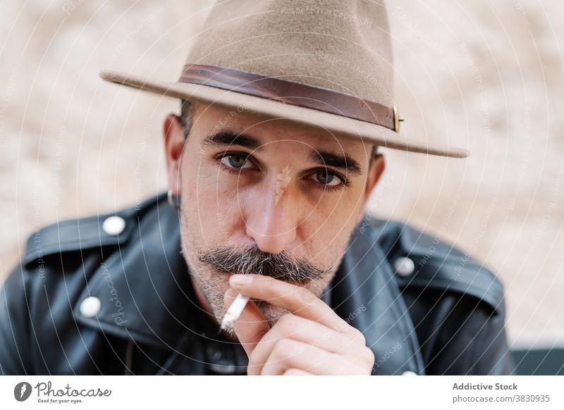 Serious pensive man in hat smoking cool smoke cigarette mustache hipster brutal rest contemplate male peaceful modern confident relax ponder concentrate
