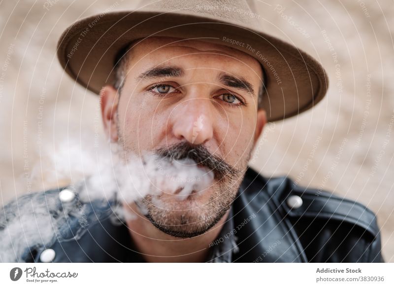 Serious pensive man in hat smoking cool smoke cigarette mustache hipster brutal rest contemplate male peaceful modern confident relax ponder concentrate