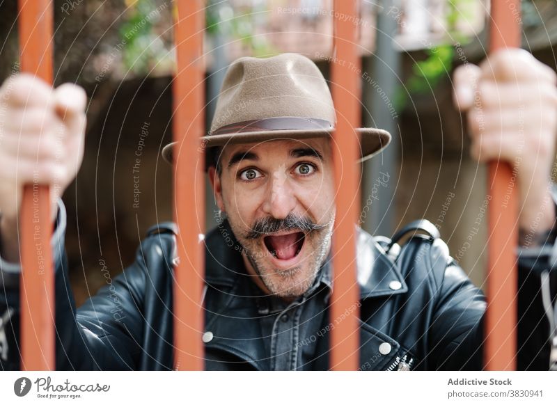 Funny hipster guy captured behind fence man fun pretend cage metrosexual bars funky excited fashion make face trendy grimace stylish mouth opened male cool