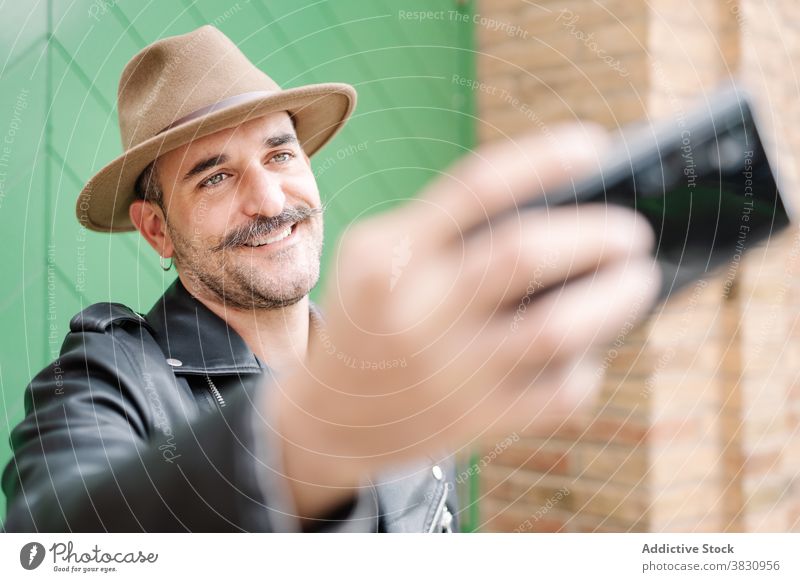 Adult man with mustache taking selfie cheerful hipster trendy beard gentleman hat metrosexual leather jacket yard content guy smartphone adult hobby