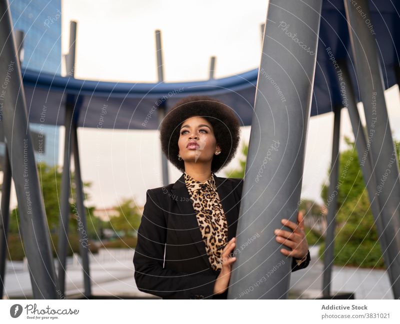 Pensive black woman leaning on metal post dreamy confident elegant think calm style peaceful serious formal female construction contemplate stand tranquil
