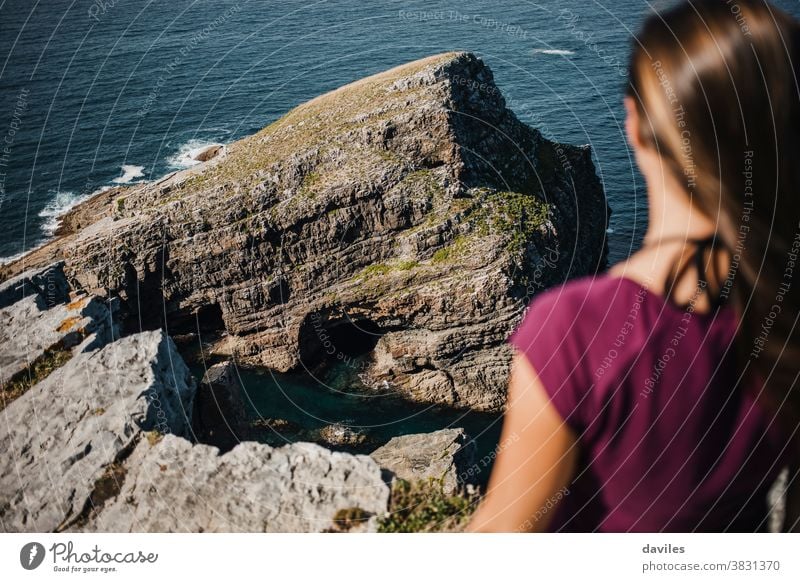 Rock and cliff in the coastline, with woman looking at it. nice inspirational pensive sightseeing traveler elevation rock purple t shirt blue earth world breath