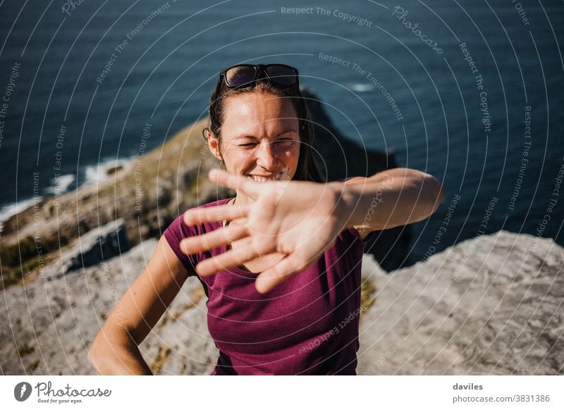 Playful woman trying to hide from photographer camera to avoid pics. mountain sea nature coast outdoors arm hand timid shame joyful playful shy expressive cover