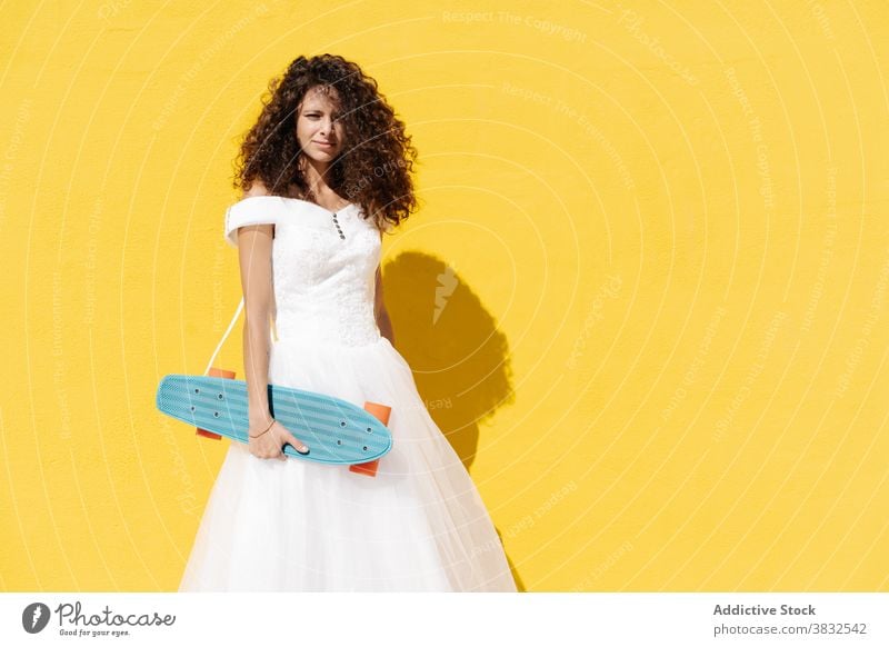 Trendy woman in bridal dress on skateboard bride cool hipster white dress wedding style cheerful vibrant happy longboard hold culture stand skater street