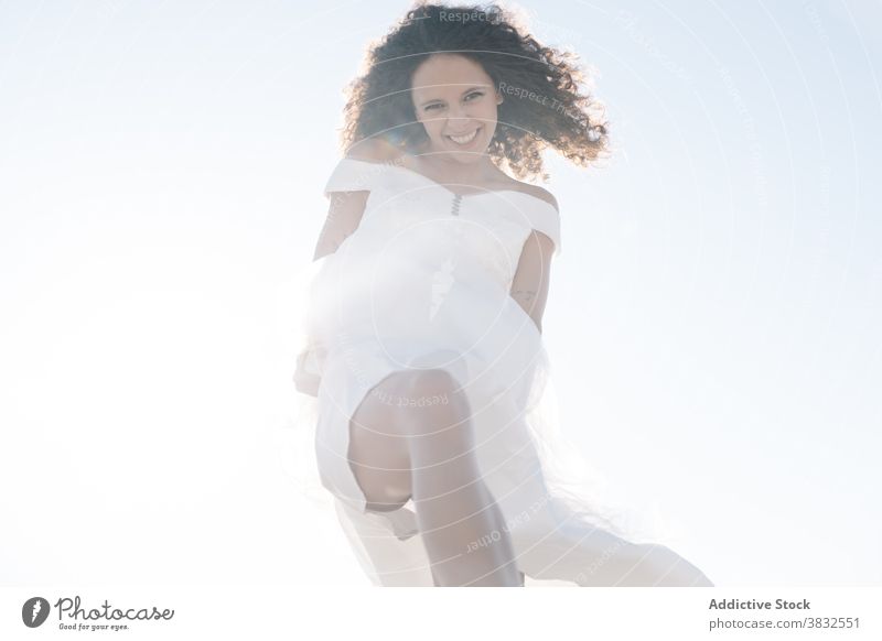 Joyful happy woman jumping looking at camera joyful freedom cool ethnic laugh white dress summer positive young cheerful fun modern healthy mixed race