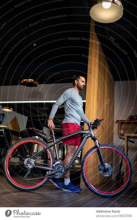 Sportsman with bicycle in gym sportsman walk training fitness prepare modern sportswear male athlete activity bike endurance power workout healthy strong