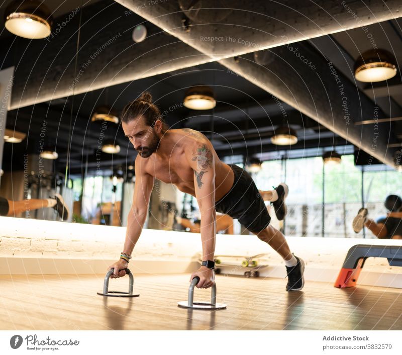Bearded sportsman exercising on push up handles gym exercise balance modern fitness training shirtless male adult athlete contemporary workout healthy power