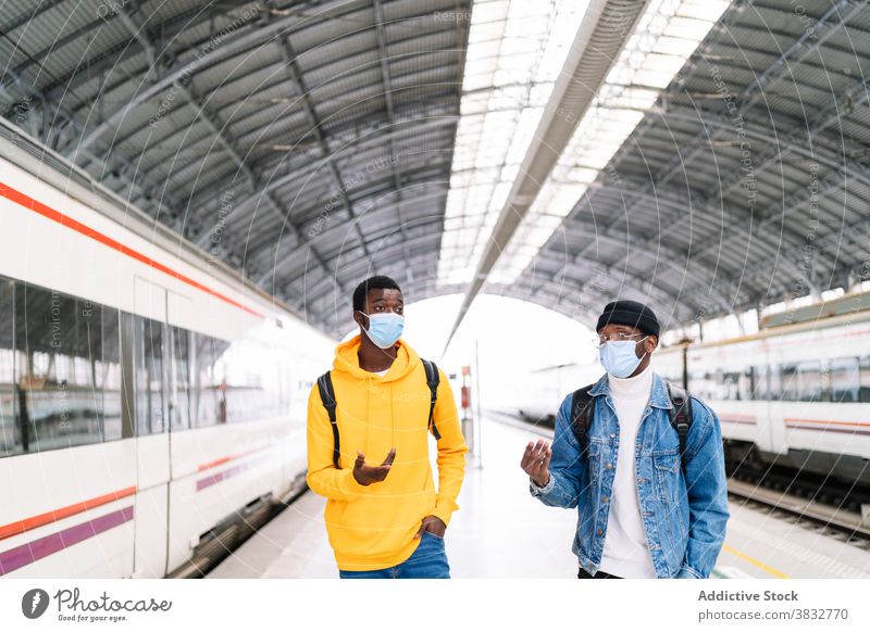 Black men in masks on train platform traveler railway station together coronavirus protect ethnic black african american talk walk transport departure modern