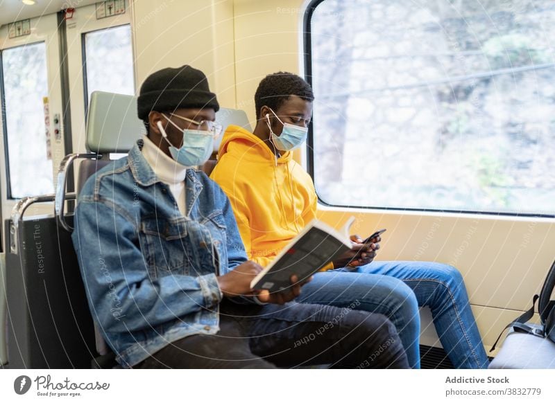 Black men riding in train during coronavirus pandemic ride passenger traveler together read book listen music ethnic black african american friend medical trip