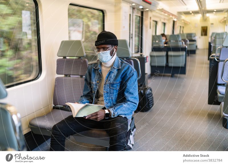 Black man in mask reading book in train travel passenger seat railroad railway coronavirus male ethnic black african american entertain medical protect prevent