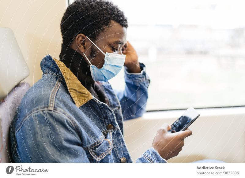 Traveling black man using cellphone in train passenger smartphone new normal travel mask coronavirus railroad railway male ethnic african american tourist