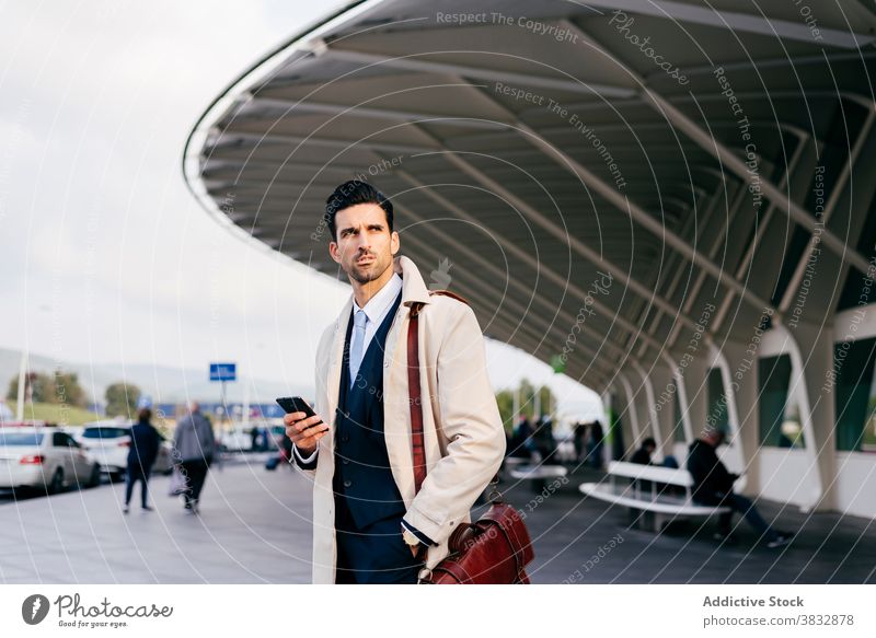 Pensive man looking away near airport with your phone in hand standing trendy watch street style businessman concentrate male thoughtful daytime ethnic pensive