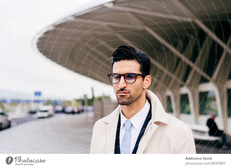 Pensive young man standing on street near modern building pensive thoughtful serious calm tranquil style trendy businessman male ethnic glasses hairstyle