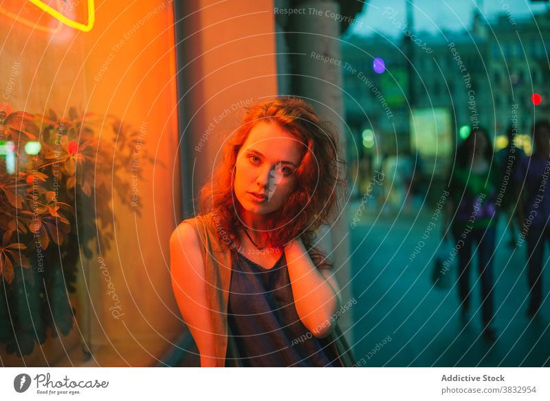 Trendy young woman standing in neon lights on city street sensual urban illuminate nightlife twilight red hair millennial curly hair female redhead evening