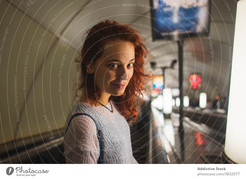 Smiling redhead woman standing on escalator subway red hair smile passenger traveler positive metro urban young female curly hair student lifestyle trip