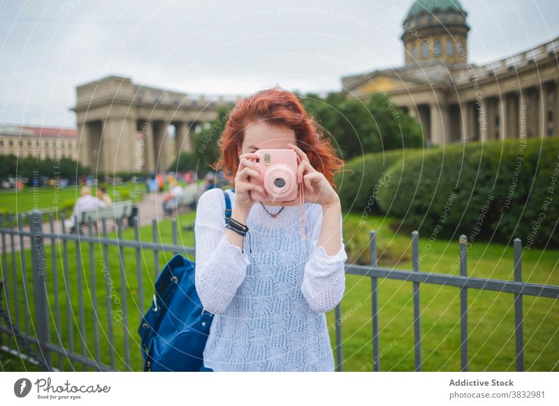 Female tourist taking photo on instant camera near old cathedral woman traveler take photo photo camera famous shoot photography sightseeing young redhead