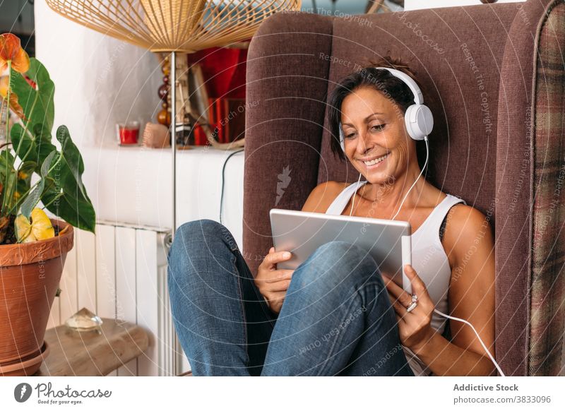 Relaxed woman with tablet and headphones chilling at home relax listen chair tranquil music adult ethnic female cozy gadget device rest comfort using lifestyle