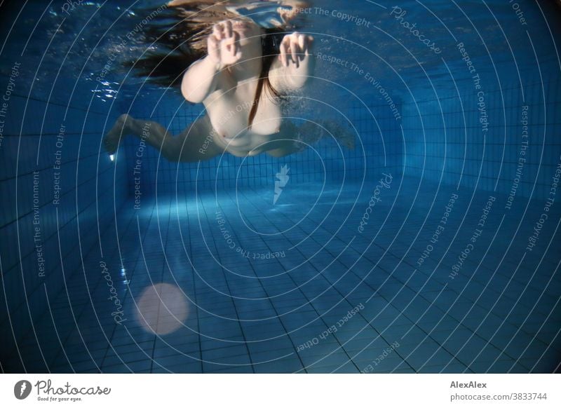 Underwater body portrait with reflection at the waterline of a young woman swimming towards the camera Young woman pale underwater pool Swimming pool