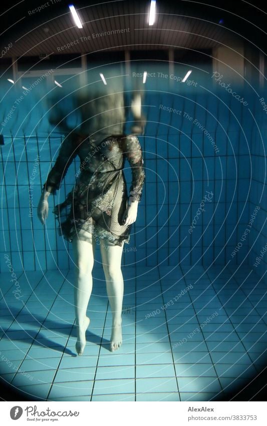 Body portrait of a young woman under water, standing in a pool, dressed in a transparent dress and bathing Young woman pale underwater Swimming pool