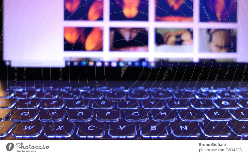 Close-up on a laptop keyboard. Erotic photos that appear on the screen in the background deliberately blurred. internet erotic online webcam chatting hand