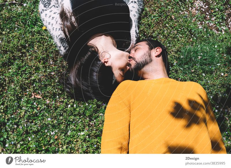 Beautiful young couple lie on the green grass in a spring meadow in the park top view. outdoor flirting hugging relationship together togetherness youth
