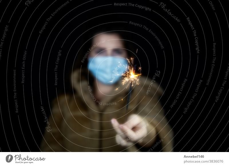 Happy new year, portrait of a young woman wearing medical mask and holding sparklers light in the dark for Covid-19, Coronavirus and New year concept