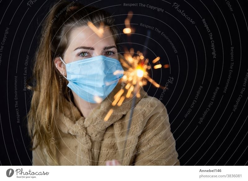 Happy new year, portrait of a young woman wearing medical mask and holding sparklers light in the dark for Covid-19, Coronavirus and New year concept