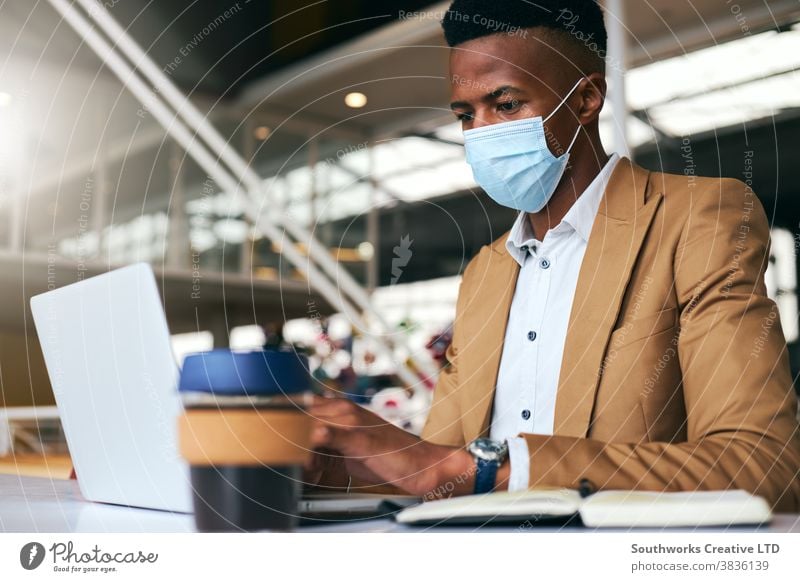 Young Businessman Wearing Mask Working On Laptop At Hot Desk In Office During Health Pandemic business businessman face mask face covering wearing ppe working