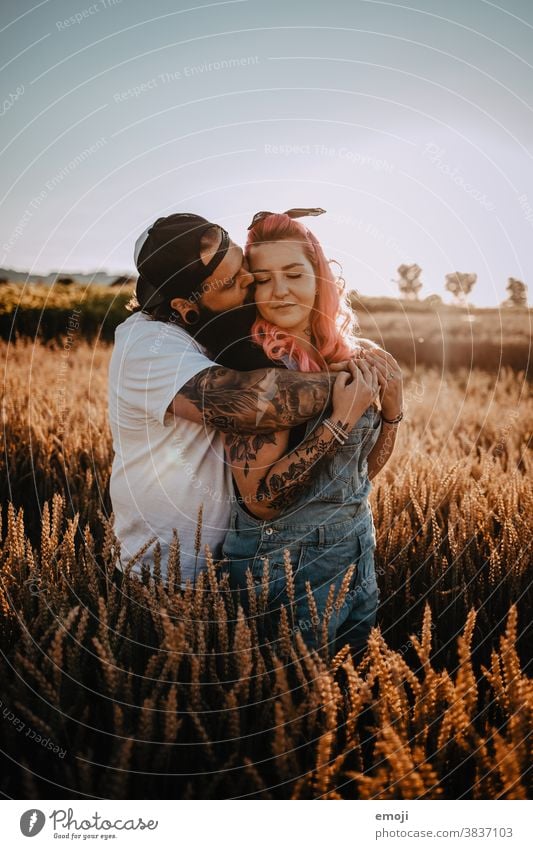Couple with tattoos and pink hair cuddling in a cornfield at sunset - a Royalty Free Stock Photo from Photocase