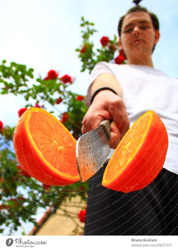 A man and an orange cut in half by a kitchen knife. Fruit full of vitamins. Vegetarian or vegan food. Deliberately blurred background. fruit fresh healthy ripe