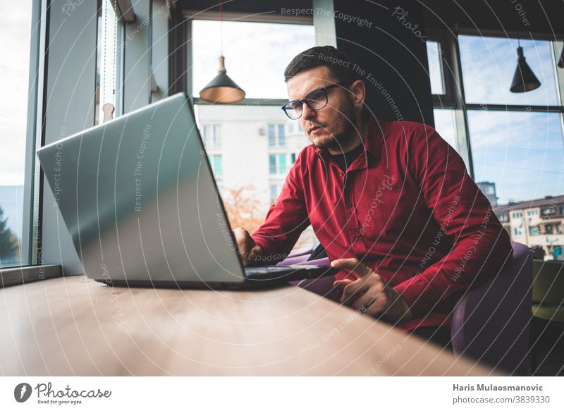 Freelancer man in red shirt with glasses working on laptop in coffee shop, remote work business businessman casual communication company owner computer